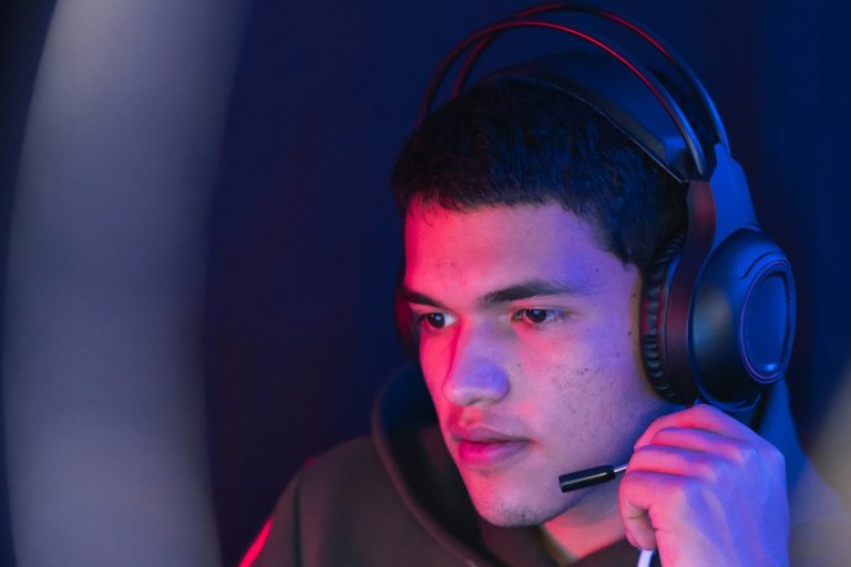 Headsets and Paging Young man focused on gaming, wearing headphones and a microphone, surrounded by blue and purple lighting.