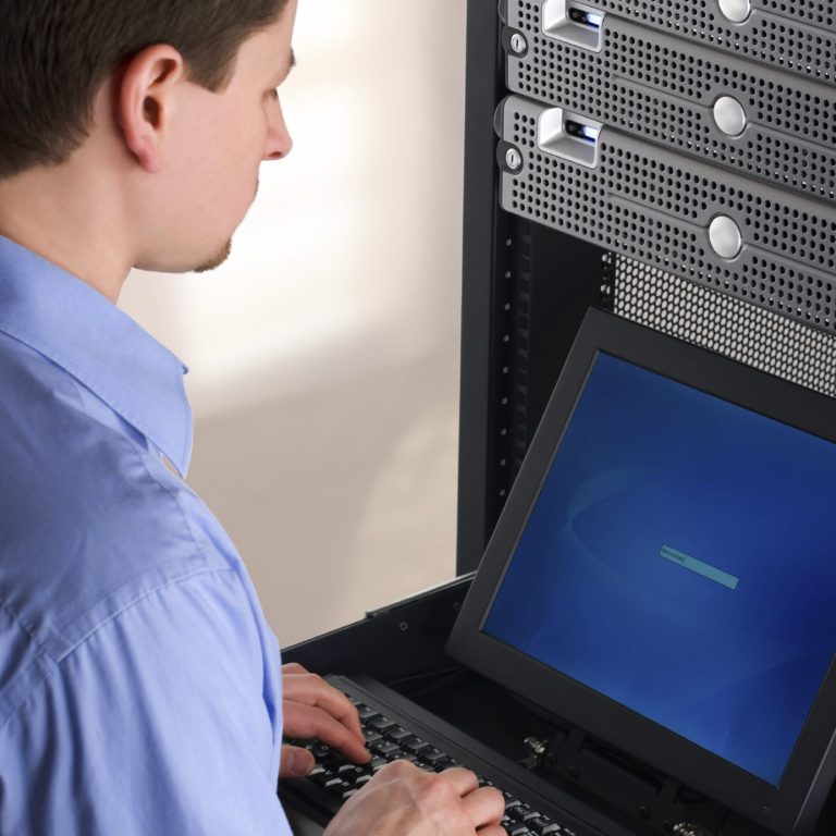 A person working on a computer in front of a server rack.