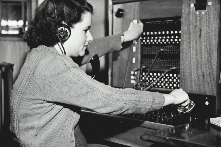 Maintenance & Support A woman operating a vintage telephone switchboard with headphones.